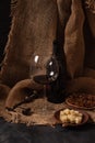 Glass and bottle of red wine with cheese, raisins, and nuts on sackcloth, dark background Royalty Free Stock Photo