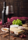 Glass and bottle of red wine with selection of various cheese on the board and grapes on wooden background. Blue Stilton, Red Royalty Free Stock Photo