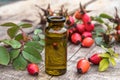 Glass bottle of rosehip seed essential oil with fresh fruits on a wooden table. Tincture or essential oil with rose hips Royalty Free Stock Photo