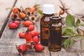 Glass bottle of rosehip seed essential oil with fresh fruits on a wooden table. Tincture or essential oil with rose hips Royalty Free Stock Photo