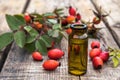 Glass bottle of rosehip seed essential oil with fresh fruits on a wooden table. Tincture or essential oil with rose hips Royalty Free Stock Photo