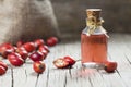 Glass bottle of rosehip seed essential oil with fresh rose hip fruits on wooden rustic background