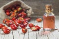 Glass bottle of rosehip seed essential oil with fresh rose hip fruits on wooden rustic background