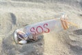 Glass bottle with seashells and message SOS on sand, closeup Royalty Free Stock Photo