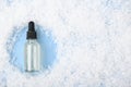 Glass bottle with serum, essential oil on blue background on the snow. Gentle moisturizing skincare product the cold winter season