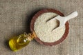 Glass bottle of sesame oil and raw sesame seeds in wooden shovel or spoon and in bowl on burlap sack Royalty Free Stock Photo