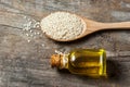 Glass bottle of sesame oil and raw sesame seeds in wooden spoon on wooden table Royalty Free Stock Photo