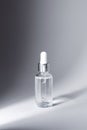 Glass bottle with silver and white pipette in ray of light on grey background mockup. Facial serum in transparent Royalty Free Stock Photo