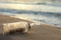 Glass bottle with SOS message on sand near sea, closeup Royalty Free Stock Photo