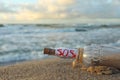 Glass bottle with SOS message on sand near sea, closeup Royalty Free Stock Photo