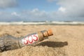 Glass bottle with SOS message on sand near sea, closeup Royalty Free Stock Photo