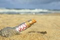 Glass bottle with SOS message on sand near sea, closeup Royalty Free Stock Photo