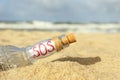 Glass bottle with SOS message on sand near sea, closeup Royalty Free Stock Photo