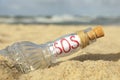 Glass bottle with SOS message on sand near sea, closeup Royalty Free Stock Photo