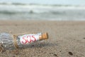 Glass bottle with SOS message on sand near sea, space for text Royalty Free Stock Photo