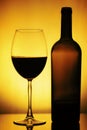 Glass and a Bottle of Wine. Bottle is open, half of it is Wine. Glass and Bottle of wine on a yellow background with a black vigne