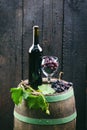 Glass and bottle of wine on a wooden barrel. Burnt, black wooden background. Vintage. Copyspace for a text. Grapes and green vine. Royalty Free Stock Photo