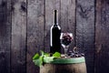 Glass and bottle of wine on a wooden barrel. Burnt, black wooden background. Vintage. Copyspace for a text. Grapes and green vine. Royalty Free Stock Photo