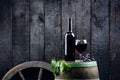 Glass and bottle of wine on a wooden barrel. Burnt, black wooden background. Vintage. Copyspace for a text. Grapes and green vine. Royalty Free Stock Photo