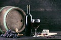 Glass and bottle of wine on a wooden barrel. Burnt, black wooden background. Vintage. Copyspace for a text. Grapes and green vine. Royalty Free Stock Photo