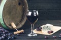 Glass and bottle of wine on a wooden barrel. Burnt, black wooden background. Vintage. Copyspace for a text. Grapes and green vine. Royalty Free Stock Photo