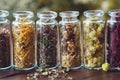 Glass bottles of dry medicinal herbs - heather, calendula, wild marjoram, daisies, helichrysum, rose petals.