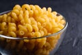 Glass bowl with cavatappi uncooked golden wheat curly pasta on textured dark black background