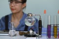 Glass bowl with cbd oil extracted from a marijuana plant on white table and female scientist conducting experiment in