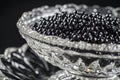 A glass bowl filled with black beads rests atop a table surface, A close-up view of luxurious black caviar nestled in a crystal