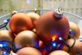 A glass bowl of mat bronze colored chtristmas balls and christmas lights