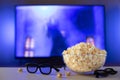 A glass bowl of popcorn, 3d glasses and remote control in the background the TV works. Evening cozy watching a movie or Royalty Free Stock Photo