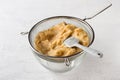 A glass bowl with pureed quince in a sieve and a silicone spatula for rubbing on a light gray background.Stage of