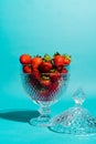 Glass bowl of red and sweet strawberries on a blue background.