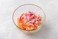 A glass bowl with shredded cabbage, grated carrots, chopped sweet peppers and pickled red onion feathers on a light gray Royalty Free Stock Photo