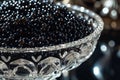 A glass bowl on a table containing black beads, A close-up view of luxurious black caviar nestled in a crystal dish, AI Generated