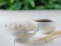 Glass bowl with white long grain rice, bowl with soy sauce and wooden sticks on white table on green tree background Royalty Free Stock Photo