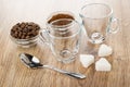Bowls with coffee beans, ground coffee, two transparent cups, pieces of sugar, spoon on wooden table Royalty Free Stock Photo