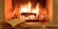 Glass of brandy and a book on burning fireplace background