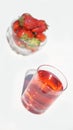 A glass of bright red raspberry-strawberry sweet cold drink with a cup of strawberries in the background Royalty Free Stock Photo