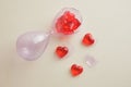 glass broken hourglass with small red glass hearts on a beige background, broken heart concept