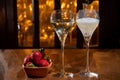 Glass of brut champagne bubbles wine in tulip glass and bowl with fresh strawberries on evening bar lights background