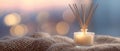 A glass candle holder with a lit candle and reed diffuser sticks on top, surrounded by soft focus bokeh lights in the background Royalty Free Stock Photo