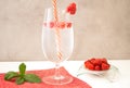 A glass of carbonated non-alcoholic raspberry drink stands on a red napkin on a white table against a gray concrete wall. Royalty Free Stock Photo
