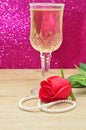 A glass of champagne displayed with a red artificial rose and a string of beads