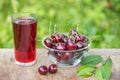 A glass of cherry juice and bowl of cherries on the table in garden outdoors Royalty Free Stock Photo