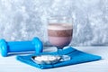 Glass of Chocolate Protein Shake with milk and black currant. L - Carnitine and blue dumbbells in background. Sport nutrition Royalty Free Stock Photo