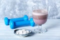 Glass of Chocolate Protein Shake with milk and black currant. L - Carnitine and blue dumbbells in background. Sport nutrition Royalty Free Stock Photo