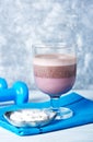 Glass of Chocolate Protein Shake with milk and black currant. L - Carnitine and blue dumbbells in background. Sport nutrition. Royalty Free Stock Photo