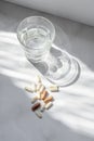 Glass with clean pure water and pills and capsule on white marble table background with aesthetic sunlignt shadow