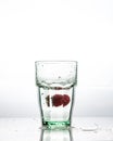 In the glass with clean and transparent water, falls fresh strawberries, splashes water.